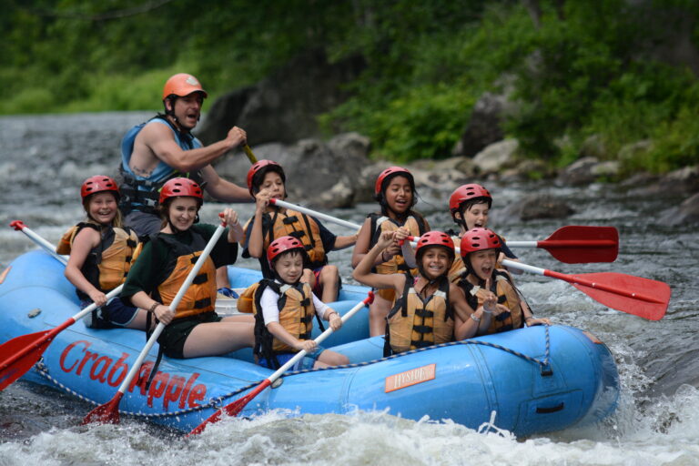 group of young rafters paddling as two girls in front link arms