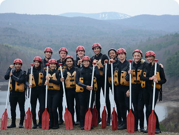 People posing in rafting gear on a hill in front of a lake