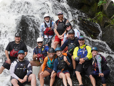 People in rafting gear posing in front of a waterfall