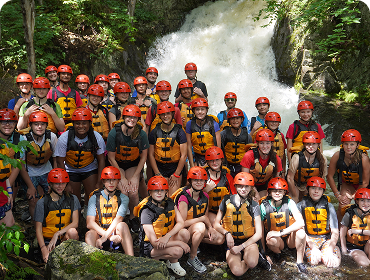 Group of young children in rafting gear posing in front of a waterfall 