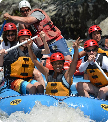People in a raft with the person in the front smiling and holding their arms up